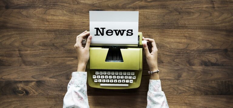 A person’s hands resting on a typewriter, which has typed the word “News” on a piece of paper.