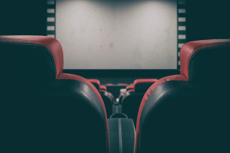 An image of a movie theater from the perspective of sitting behind the theater seats.