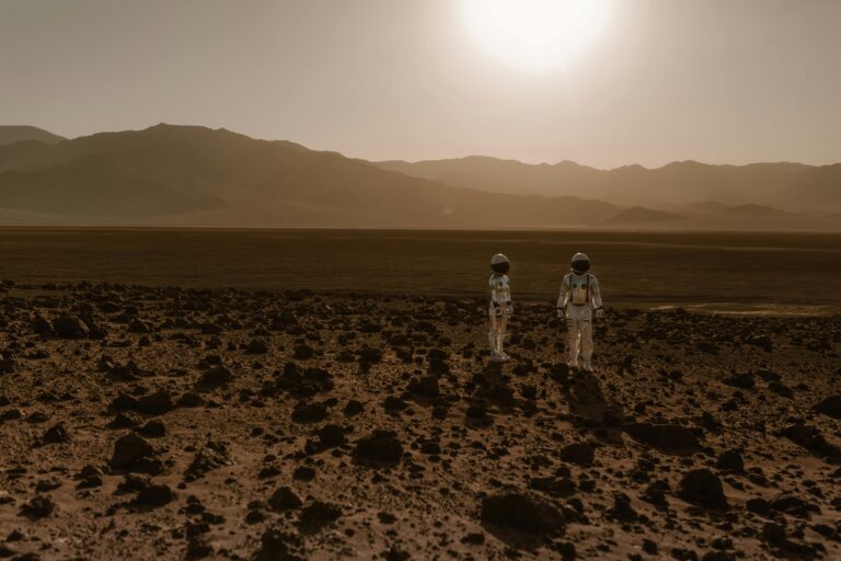 Two astronauts stand in the middle of a rocky, red, “Martian-like” desert.