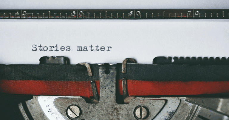 “Stories matter” is typed onto white paper that is sticking out of the top of a black and red typewriter.