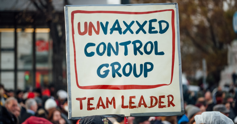 Cardboard sign held during a protest march, saying ‘Unvaxxed control group team leader’.