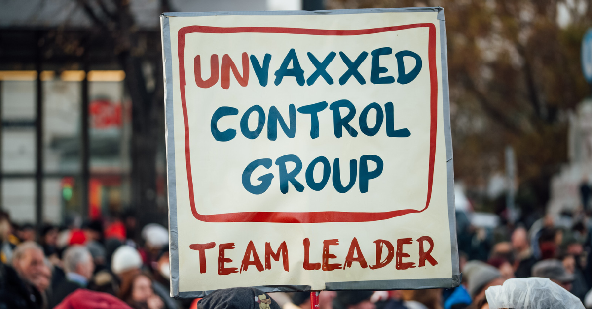 Cardboard sign held during a protest march, saying ‘Unvaxxed control group team leader’.