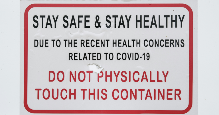 A sign mounted on a wall reading "Stay safe & stay healthy. Due to the recent health concerns related to COVID-19. Do not physically touch this container."