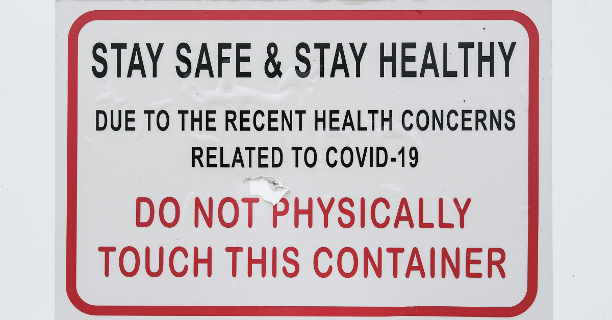 A sign mounted on a wall reading "Stay safe & stay healthy. Due to the recent health concerns related to COVID-19. Do not physically touch this container."